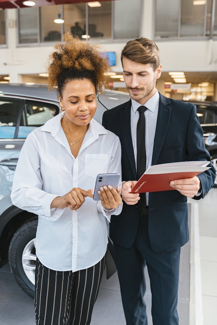 services-03 A man and woman reviewing car options on a mobile phone in a dealership showroom.